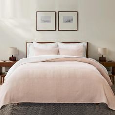 a bed with two pictures on the wall above it and a pink comforter set