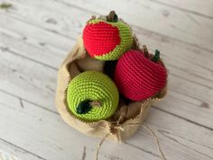 three crocheted apples in a bag on a white wooden table with twine