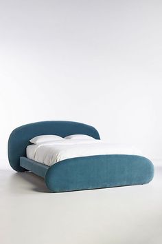 a blue bed with white sheets and pillows on top of it, in front of a white wall