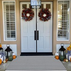 two wreaths on the front door of a house with pumpkins and gourds