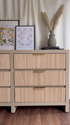 a wooden dresser with two pictures on top of it and a vase next to it