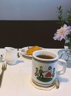 there is a cup of tea on the table next to some silverware and flowers