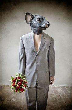 a man in a suit with a rat mask on his head holding a bouquet of flowers