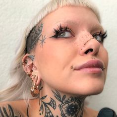 a woman with tattoos and piercings on her face looks up at the camera while wearing ear rings