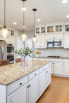 a large kitchen with white cabinets and marble counter tops, along with wooden flooring