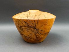 a wooden bowl sitting on top of a gray table next to a black wall and floor