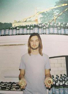 a man holding two bananas in front of a wall full of beer bottles and cans