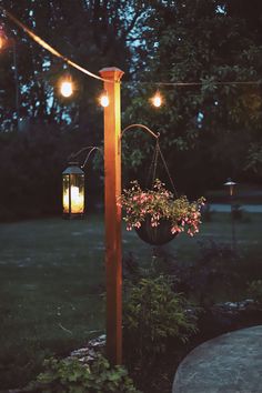 some lights hanging from a pole in the middle of a yard with flowers on it