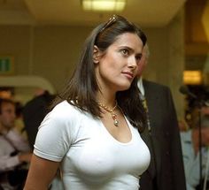 a woman wearing a white shirt and gold necklace standing in front of a group of people