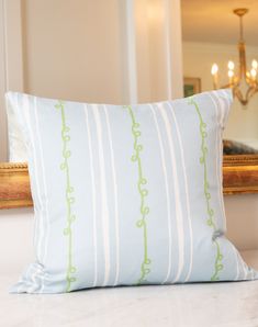 a white and green striped pillow sitting on top of a bed next to a mirror