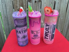 three different types of drinks on a red tablecloth next to a fence and wooden posts