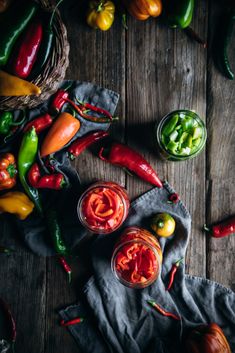 several different types of peppers on a table with some sauce in the bowl and two small bowls next to them