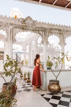 a woman in a red dress is standing at the edge of a gazebo with potted plants