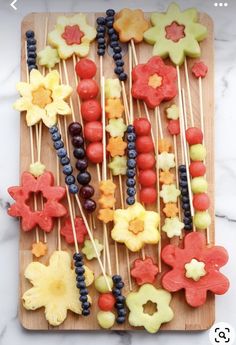 a wooden cutting board topped with fruit and veggies on skewered sticks