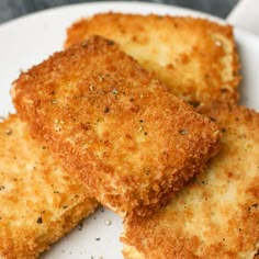 three pieces of fried cheese on a white plate with seasoning sprinkles