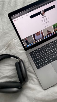 an open laptop computer sitting on top of a bed next to headphones and a phone