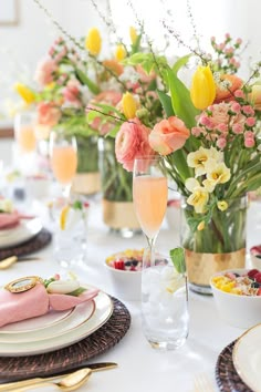 the table is set with plates, glasses and vases full of flowers on it