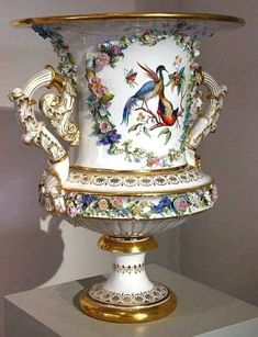 an elaborately decorated vase sitting on top of a white pedestal with gold trimming