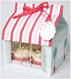 a paper house with cupcakes in the window and a red ribbon on top