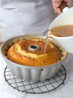 a person pours syrup into a bundt cake in a pan on a wire rack