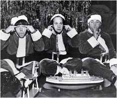 three men dressed as santa clause sitting on a couch in front of a christmas tree