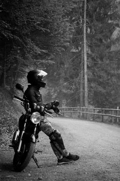 a person sitting on a motorcycle in the middle of a road with trees behind them