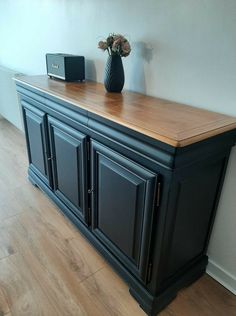 a large black cabinet with wooden top and drawers on the bottom, in front of a white wall