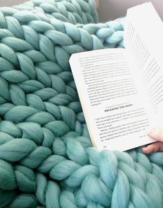 a person is reading a book while laying on a large chunky knitted blanket