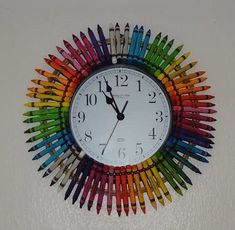 a clock made out of colored crayons on the side of a white wall