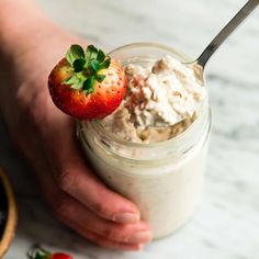 a person holding a strawberry and cream in a jar with strawberries on the side