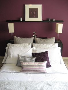 a bed with white sheets and pillows in front of a purple wall, two framed pictures above the headboard