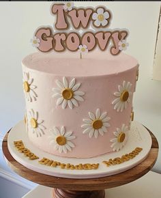 a pink cake with daisies on top sitting on a table