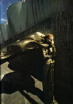 a woman standing next to a wall covered in a gold cloth with her hands on her head