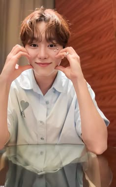 a young boy sitting at a table with his hands on his face and looking into the camera