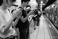 people standing in line waiting to get on the subway train and use their cell phones