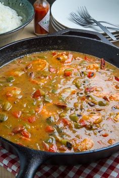 a pan filled with soup next to rice and spoons on top of a table