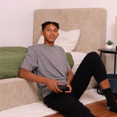 a young man sitting on the floor with a remote control in his hand and looking at the camera