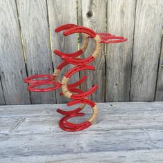 a red sculpture on top of a wooden table next to a wood fence and wall