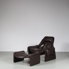 a brown leather chair and footstool in front of a white wall