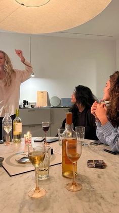 three women sitting at a table with wine glasses and bottles in front of them,