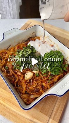 someone is pouring water into a dish with noodles and vegetables in it on a cutting board