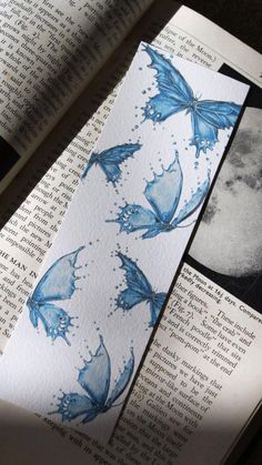 an open book with blue butterflies on it and the pages are covered in watercolor