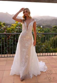 a woman in a wedding dress standing on a balcony looking at the camera with mountains in the background