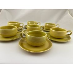 a group of yellow cups and saucers on a white tablecloth with a white background