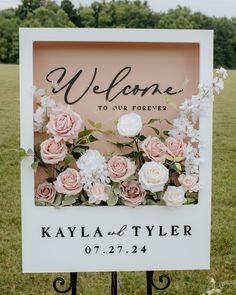 a welcome sign with flowers and greenery on it in front of a grassy field