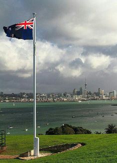 an australian flag flying in front of the ocean and cityscape on a cloudy day