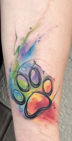 a colorful paw tattoo on the left inner arm with watercolor paint splatters