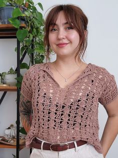 a woman standing in front of a potted plant wearing a crochet top