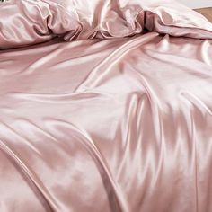 an unmade bed with pink sheets and pillows on top of it, next to a night stand