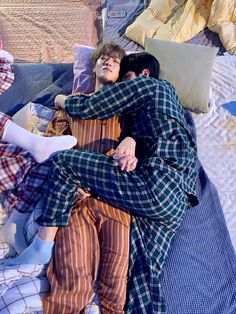 two people laying on top of a bed covered in blankets and pillows next to each other